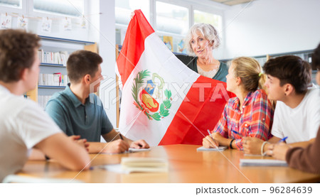 Pupils sitting in class and listening carefully to female teacher holding Peru flag in hands and talking about geography and history of countries in library 96284639