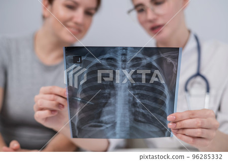The doctor consults a caucasian woman and comments on the x-ray of the lungs.  96285332