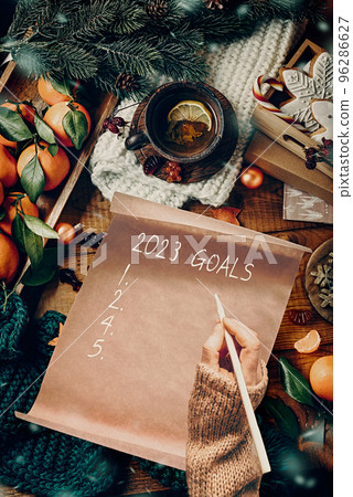 Woman writes on craft paper with Christmas decor, top view. New Year's goals Woman writes on craft paper with Christmas decor, top view. New Year's goals 96286627