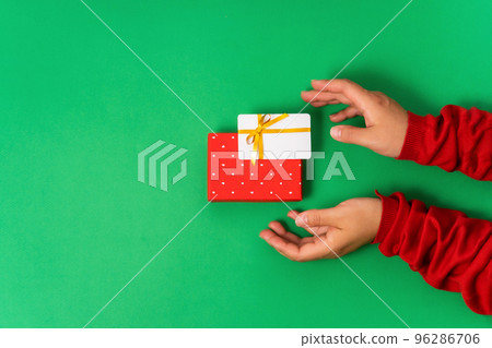 Female hands hold a levitating Bonus or gift bank card and a box with a gift. Top view, green background 96286706