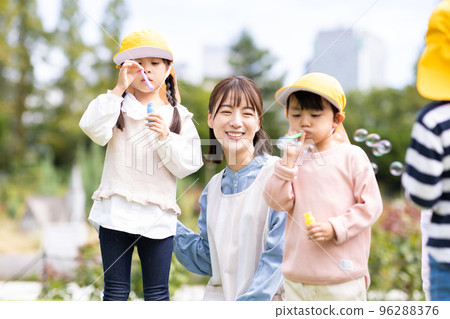 Nursery teacher and kindergarten children playing in the park 96288376
