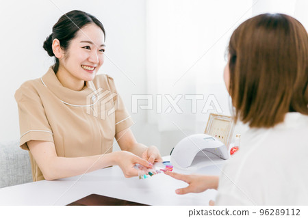 Manicurist and Asian woman counseling color and design using nail tips at nail salon 96289112