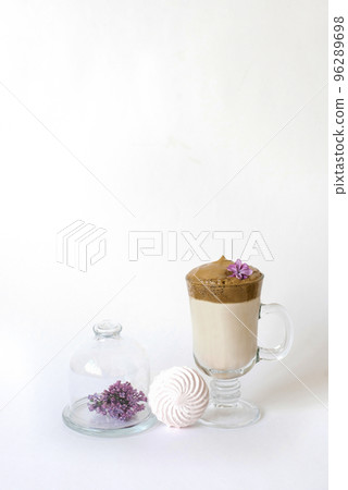 Dalgona coffee in a transparent mug with a lilac flower on a white background and a sprig of lilac lying on a serving plate and marshmallows. Spring or summer drinks menu Dalgona coffee in a transparent mug with a lilac flower on a white background and a sprig of lilac lying on a serving plate and marshmallows. Spring or summer drinks menu 96289698