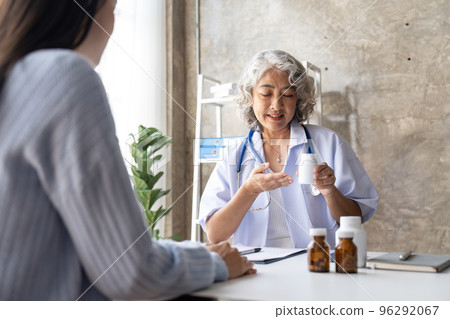 Senior doctor woman holding a pill bottle while talking with a patient and reviewing his medication at office room. Senior doctor woman holding a pill bottle while talking with a patient and reviewing his medication at office room. 96292067
