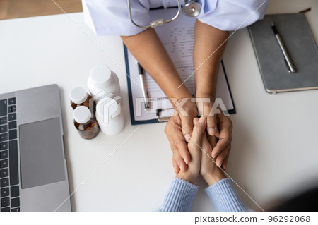 Doctor giving hope. Close up shot of young female physician leaning forward to smiling elderly lady patient holding her hand in palms. Woman caretaker in white coat supporting encouraging old person 96292068