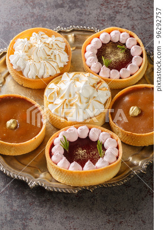 set of sweet tartlets for the holiday with lemon curd, raspberry curd, nuts and chocolate close-up on a plate. Vertical set of sweet tartlets for the holiday with lemon curd, raspberry curd, nuts and chocolate close-up on a plate. Vertical 96292757