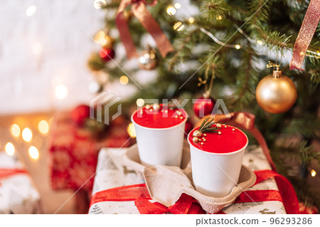 Takeaway cake in white disposable cups on gift boxes in front of Christmas tree 96293286