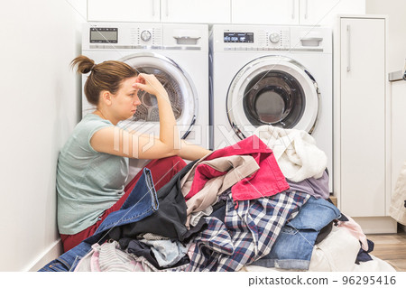 Upset woman in laudry room sitting ona floor with dirty clothes Upset woman in laudry room sitting ona floor with dirty clothes 96295416
