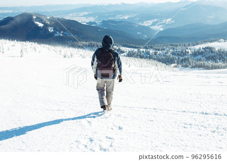 Man with backpack trekking in mountains. Cold weather, snow on hills. Winter hiking. 96295616