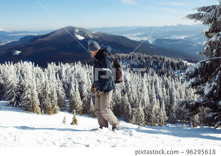 Man with backpack trekking in mountains. Cold weather, snow on hills. Winter hiking. 96295618