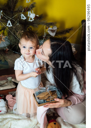 Boxing day and unpacking Christmas gift boxes. Cute Little baby toddler girl and mom unpack gift boxes near the Christmas tree at home. Merry Christmas and a Happy New Year 96296495
