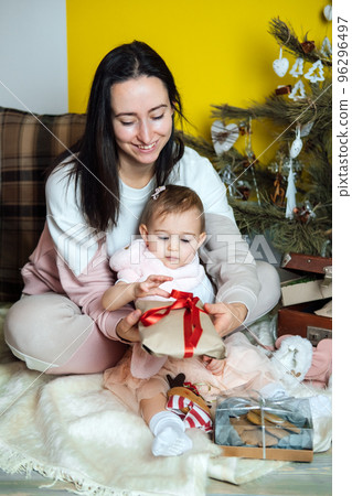 Boxing day and unpacking Christmas gift boxes. Cute Little baby toddler girl and mom unpack gift boxes near the Christmas tree at home. Merry Christmas and a Happy New Year 96296497