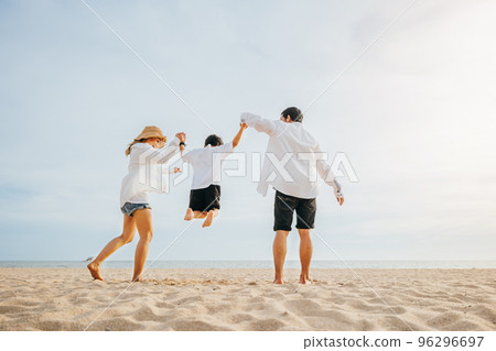 Happy Asian family have fun and live healthy lifestyle together on beach, Back family mother, father and son holding hands and jumping in air at dawn time, Family outdoor activities concept 96296697