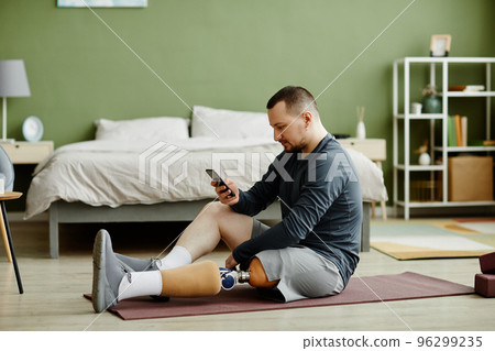 Man with prosthetic leg sitting on yoga mat Man with prosthetic leg sitting on yoga mat 96299235