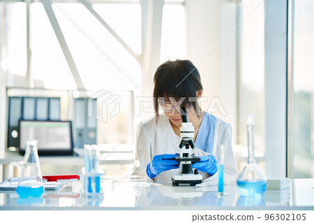 Scientist looking through a microscope working in science laboratory Scientist looking through a microscope working in science laboratory 96302105