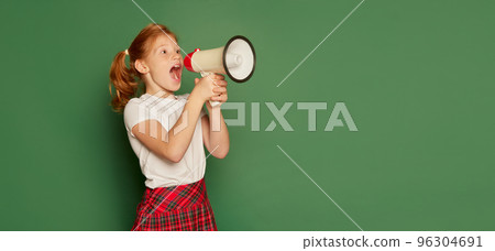 Back to school concept. Happy pupil of elementary school wearing modern school uniform isolated over dark green background. Happy charming girl, kid with megaphone 96304691