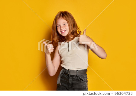 Nice, ok. Portrait of little stylish girl with long red hair and freckles isolated over bright yellow background. Concept of children emotions, dance, music, happiness 96304723