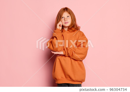 Portriat of little girl, charming kid with long red hair and freckles posing isolated over pink background. Concept of children emotions, casual sports fashion style 96304734