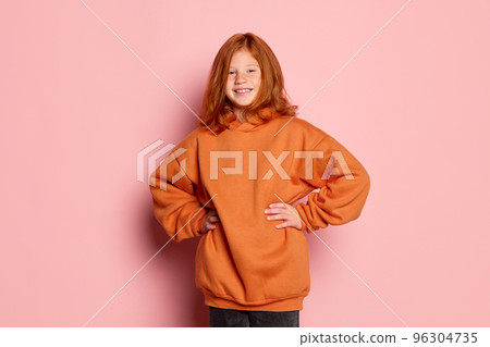 Happy school age girl, emotional kid with long red hair and freckles posing isolated over pink background. Concept of children emotions, casual sports fashion style 96304735