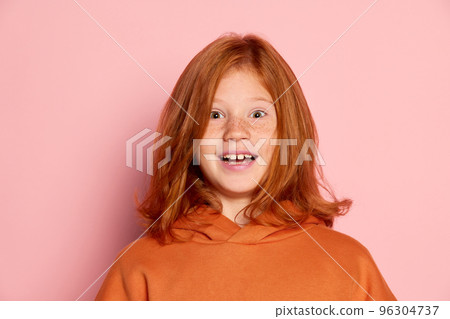 Smiling teen girl, emotional kid with long red hair and freckles posing isolated over pink background. Concept of children emotions, casual sports fashion style 96304737