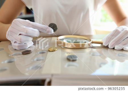 Female numismatist examines collection of coins. Female numismatist examines collection of coins. 96305235