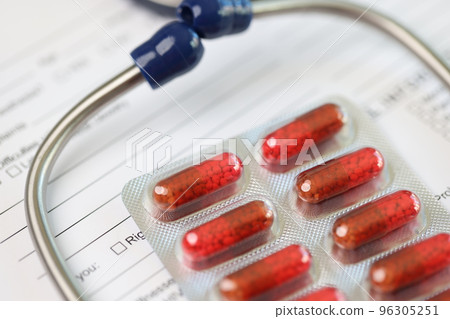 Stethoscope with red pills and medical insurance application form or laboratory tests close-up. 96305251