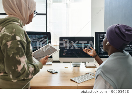 Young confident African American IT engineer making presentation of decoded data on computer screen to female colleague in hijab Young confident African American IT engineer making presentation of decoded data on computer screen to female colleague in hijab 96305438