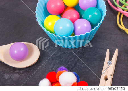 Colorful pompoms, balls and rubber erasers with spoon and tongs. Development of kids motor skills Colorful pompoms, balls and rubber erasers with spoon and tongs. Development of kids motor skills 96305450