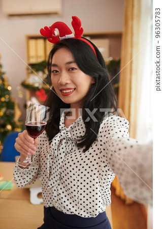 Portrait of cheerful female entrepreneur holding glass of wine when taking selfie in office decorated for Christmas 96305783