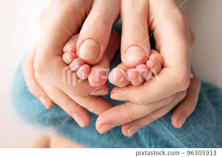 Mother is doing massage on her baby foot. Close up baby feet in mother hands on a blue background. Prevention of flat feet, development, muscle tone, dysplasia. Family, love, care, and health concept 96305913