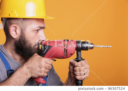 Professional builder drilling holes with electric nail gun, using power drill to work on house refurbishment. Construction worker repairman holding drilling tool in studio shot. 96307524