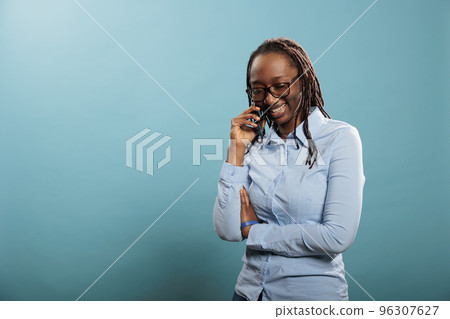 Happy joyful young woman smiling heartily while having a phone call conversation on blue background. Cheerful adult person talking with friend on touchscreen cellphone device. Happy joyful young woman smiling heartily while having a phone call conversation on blue background. Cheerful adult person talking with friend on touchscreen cellphone device. 96307627