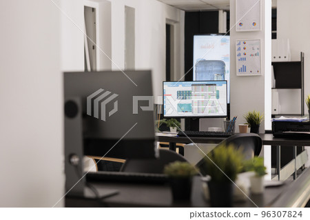 Workstations with desktop devices on wooden desks in contemporary coworking office. Empty workspace before staff arrives to work early in the morning, indoor working concept. Workstations with desktop devices on wooden desks in contemporary coworking office. Empty workspace before staff arrives to work early in the morning, indoor working concept. 96307824