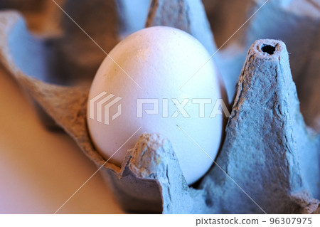 Close-up of one whiteegg in a paper tray. Minimalism on a white background. Eggs contain vitamins, phosphorus, zinc and a lot of choline. Recyclable materials egg container. 96307975