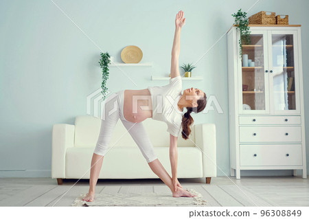 Pregnant woman does utthita trikonasana near sofa at home Pregnant woman does utthita trikonasana near sofa at home 96308849