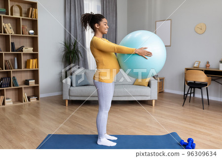 Smiling young black pregnant woman future mother with big belly practicing yoga on mat with fitness ball 96309634