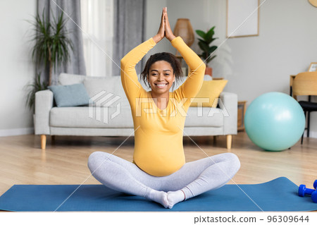 Smiling young black pregnant female with big belly sit, practicing yoga on mat, enjoy workout at spare time 96309644