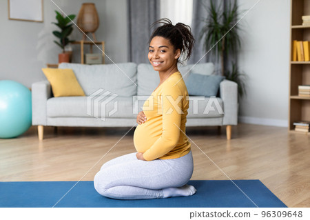 Smiling young black pregnant lady touch big belly, doing exercises, practicing yoga, enjoys baby movements 96309648