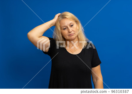 Hmm, I need to think.Pensive confused caucasian blonde woman scratching her head in doubt, not sure contemplating with a puzzled uncertain face. Indoor studio shot isolated on blue background. 96310387