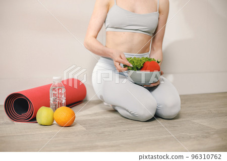 Fit woman with lots of healthy fresh food at home. Cropped view of woman wearing grey leggins. Concept of losing weight, sports and healthy eating. 96310762