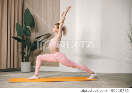 Sporty young woman training at home. Woman wearing rose top and leggins. Woman doing yoga on an orange mat. Sporty young woman training at home. Woman wearing rose top and leggins. Woman doing yoga on an orange mat. 96310785