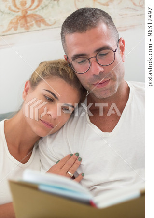Focused man and woman lying in bed and reading book in morning 96312497