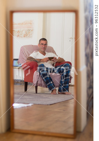 Reflection in mirror of man sitting in armchair in morning Reflection in mirror of man sitting in armchair in morning 96312532