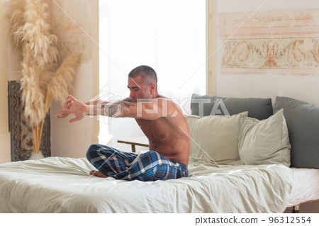 Man sitting on bed and stretching arms in morning Man sitting on bed and stretching arms in morning 96312554