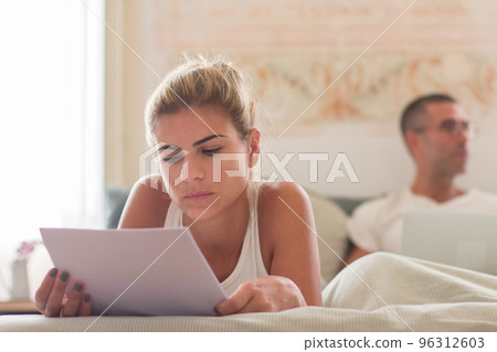 Woman looking at sheets of paper while lying in bed in morning 96312603