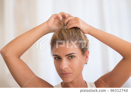 Cheerful woman making bun hairstyle and looking at camera 96312748