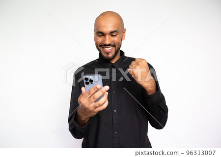 Portrait of happy young man with phone making winning gesture 96313007