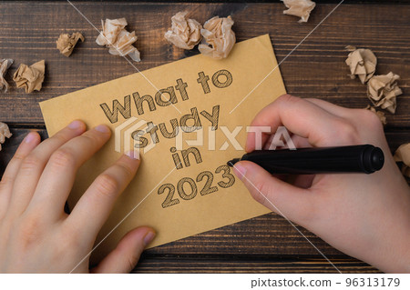 Person writes text What to Study in 2023 at wooden table 96313179
