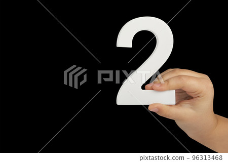 Close-up hand holding a white number 2 on a black background. Number two isolate on black background in child's hand. 96313468