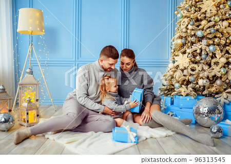 Happy family little girl, mather and father opening gift box near Christmas tree in living room  96313545
